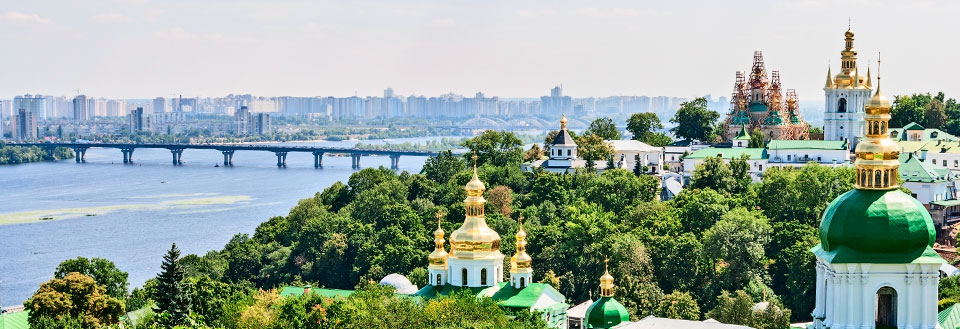 Panoramaudsigt over en by med floden, broer, moderne bygninger og kirker med gyldne kupler.