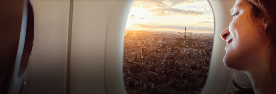 En kvinde ser ud af flyets vindue på bylandskabet og solnedgangen.