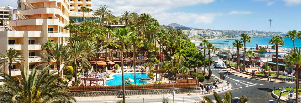 Billede af et feriested på Maspalomas med palmer, en swimmingpool og folk, der nyder solen. Havet i baggrunden.