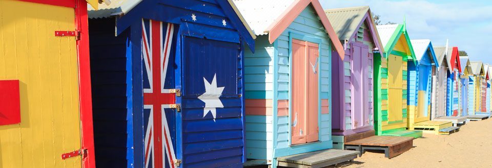 Farverige strandhytter i træ står på en række med det australske flag malet på en af dem.