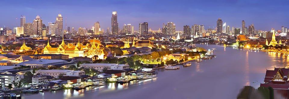 Panoramaudsigt over Bangkok ved aftenstid med oplyste bygninger og Chao Praya-floden, der skærer gennem byen.