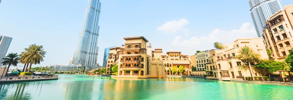 Billede af Dubai med høje skyskrabere ved en kunstig sø omgivet af palmetræer under en klar blå himmel.