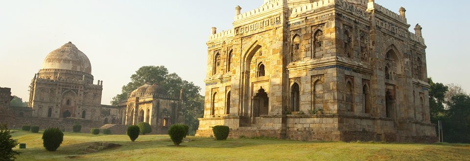 Billedet viser gamle stenstrukturer med indgange og komplicerede mønstre omgivet af grønne græsplæner i Lodhi Gardens i Delhi.
