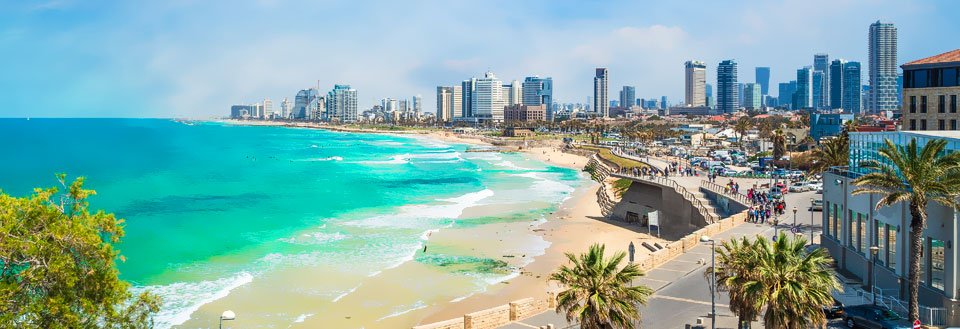 Billede af en livlig strandpromenade i Tel Aviv med blåt hav, sandstrand og moderne bysilhuet i baggrunden.