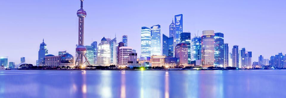 Billede af Shanghais skyline ved vandkanten i skumringen med oplyste bygninger og et karakteristisk tårn.