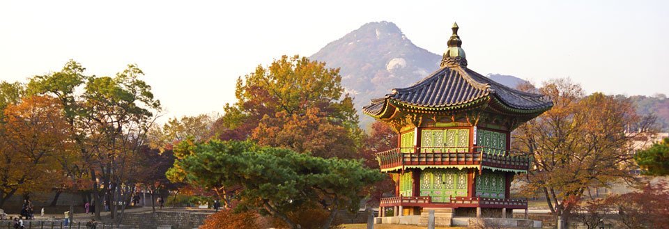 Billedet viser et farverigt traditionelt asiatisk tempel blandt efterårstræer med et bjerg i baggrunden.