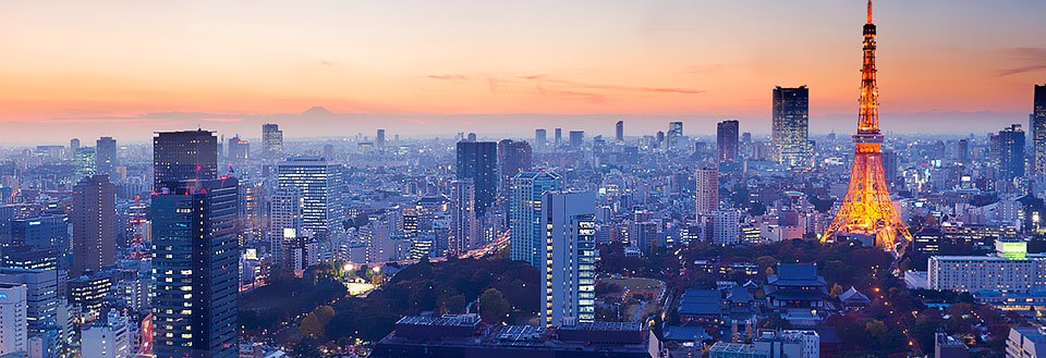 Skumring over Tokyo med moderne bygninger og en ikonisk tårnlignende struktur belyst i forgrunden.