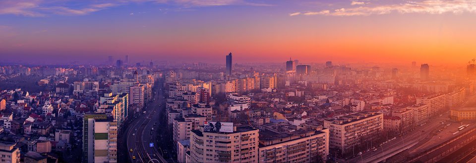Billede af Bukarest ved solnedgang med højhuse og en travl hovedvej.