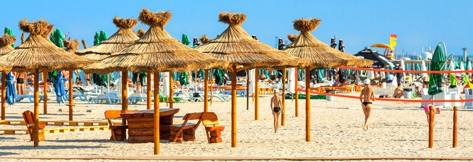 En solrig strandpromenade i Constanta med parasoller af strå og træmøbler. Folk solbader og nyder vejret.