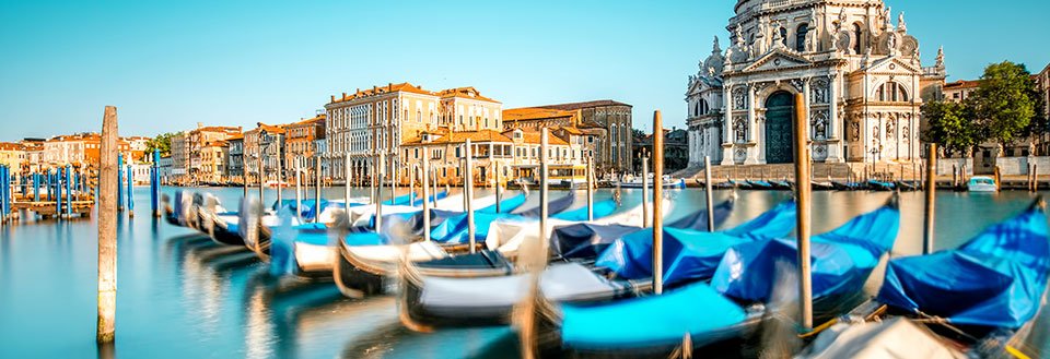 Billede af gondoler på det rolige vand i Venedig, med historiske bygninger i baggrunden.
