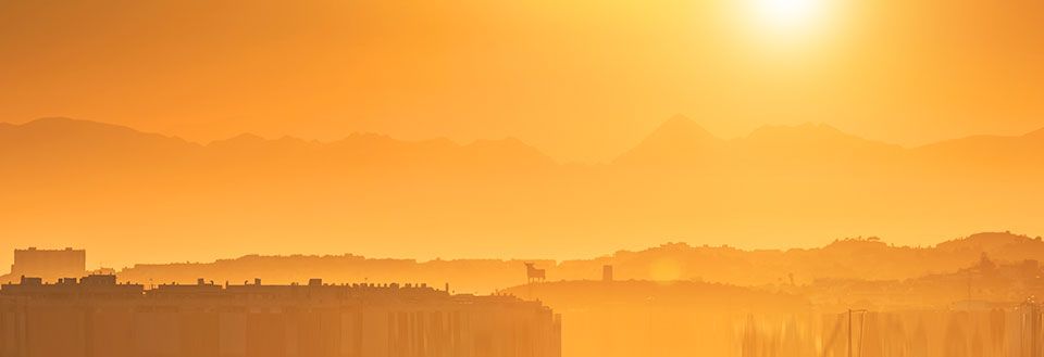 En solnedgang skaber silhuetter af en byskyline mod et bjergrigt baggrundstæppe, badet i gyldent lys.