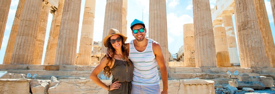 To smilende personer foran de gamle ruiner af Parthenon på Akropolis i Athen.