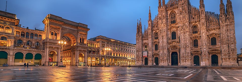 Et aftensbillede af Domkirken i Milano med en øde plads og belyste bygninger.