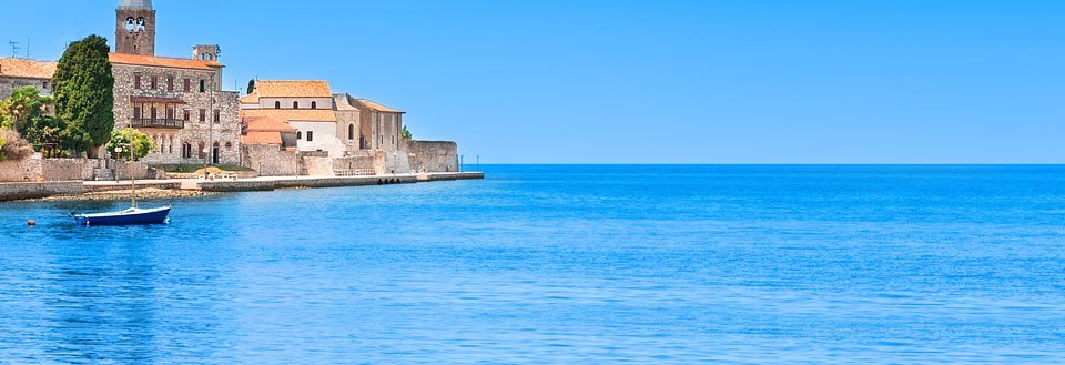 En fredelig kystlinje med gamle bygninger og en enkelt blå båd på det rolige hav.