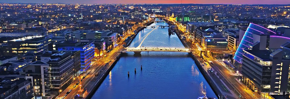 En aftenudsigt over Dublin med oplyste bygninger og Liffeyfloden, der snor sig igennem bylandskabet.