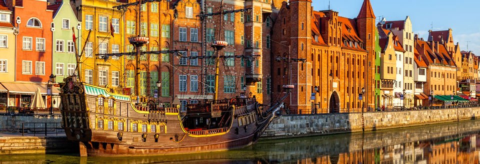 Farverige bygninger afspejler sig i vandet i Gdansk ved siden af et gammelt sejlskib i havnen.