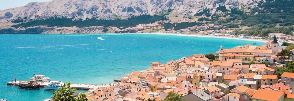 Kystbyen Krk med terrakottatage, omgivet af bjerge og klart blåt hav.