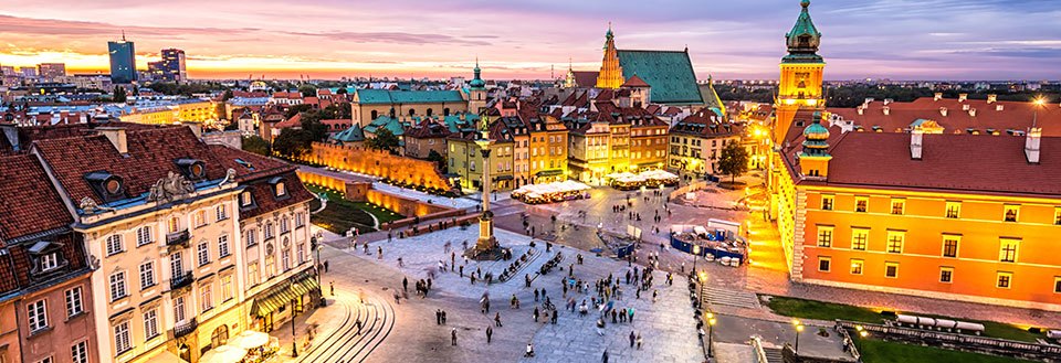 Farverig solnedgang over en historisk byplads i Warszawa med mennesker og traditionelle bygninger.