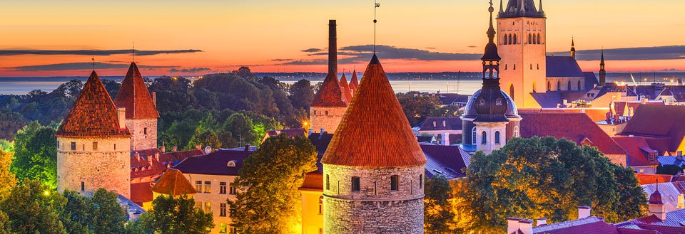 Aftenbillede af Tallinn med tårne og spir mod en solnedgangsbaggrund.