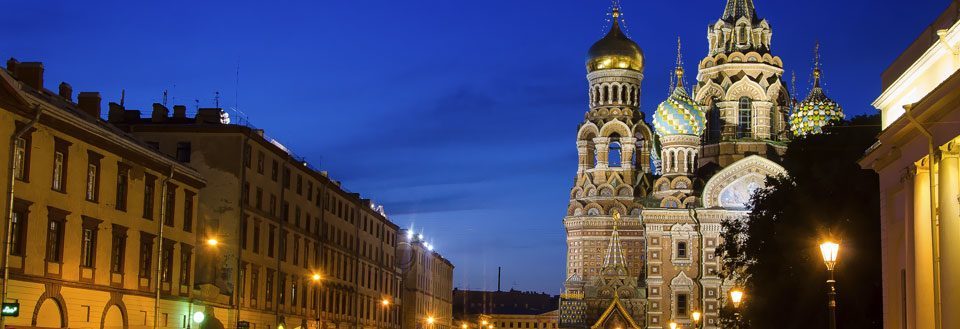 Aftenbillede af bygader med en ikonisk kuppelbelagt kirke oplyst i baggrunden.
