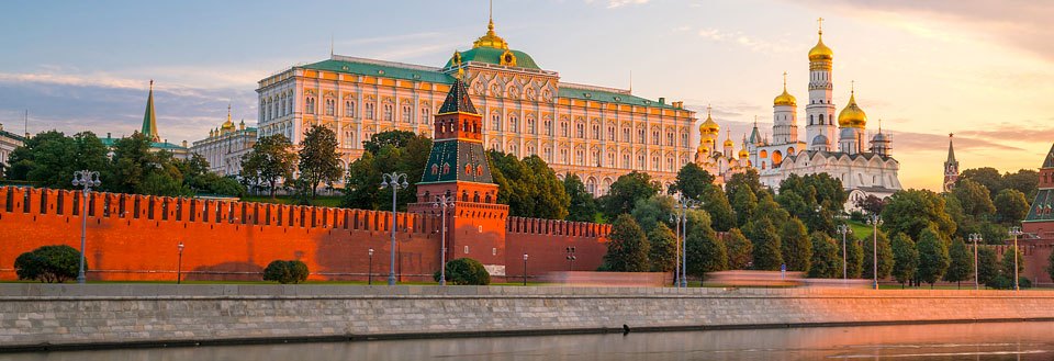 Billede af Kreml i Moskva ved floden, med røde mure og gyldne tårne under aftensolen.