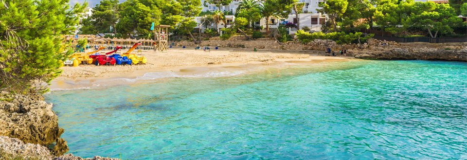 Billedet viser en idyllisk strand med turkisblåt vand, farverige strandstole og frodige træer ved kysten.