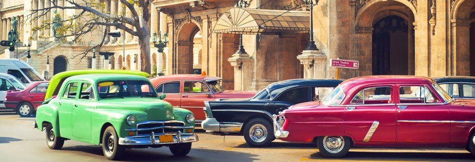 Farverige vintagebiler holder parkeret på en gade med historiske bygninger i baggrunden.