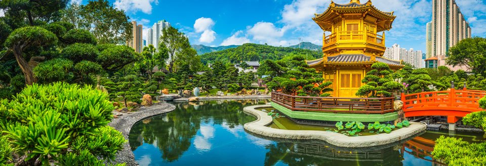 Panorama af en fredfyldt japansk have med en gylden pagode, en rød bro, en dam og frodig vegetation mod højhuse.
