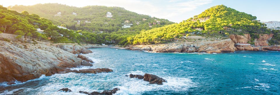 Billede af en malerisk kystlinje med klippefyldte strande og grønne bakker med bygninger.