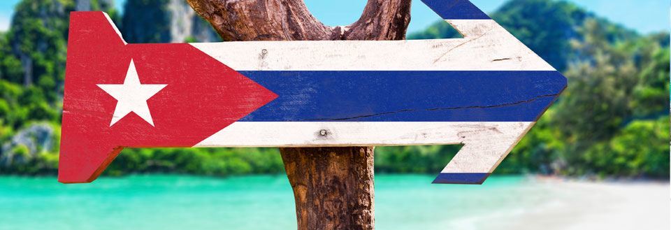 Træskilt malet som Cubas flag peger til højre foran tropisk landskab.