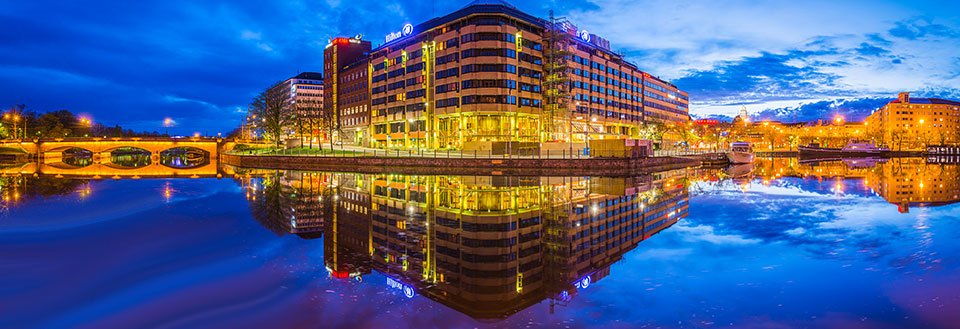 Et moderne bylandskab ved en flod i skumringen med spejlinger af bygningerne i vandet.