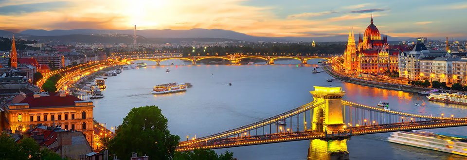 Oplyst bro og parlamentsbygningen ved floden i Budapest ved tusmørke.