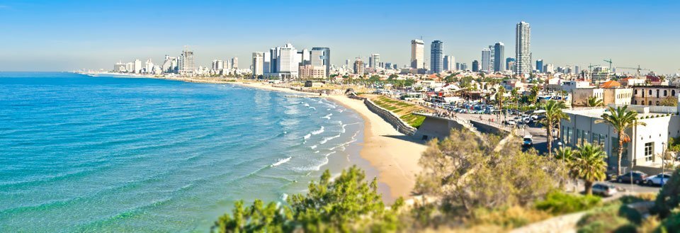 Panoramaudsigt over en kystby med højhuse langs strandpromenaden og klart blåt hav.