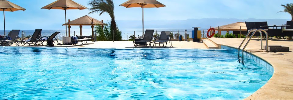 Et luksuriøst poolområde med liggestole og parasoller under en klar blå himmel.