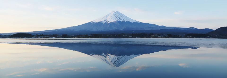 Billedet viser det snebeklædte Mount Fuji spejlet i vandet ved skumring.