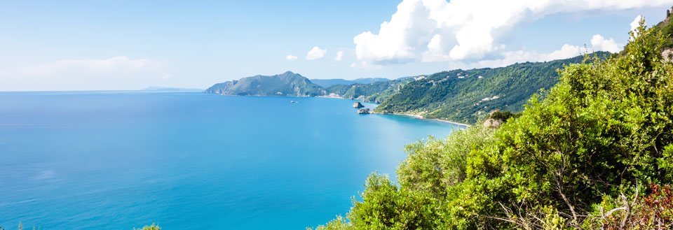 Billedet viser et panorama over et blåt hav med grønne skråninger i forgrunden og bjerge i baggrunden.