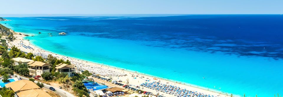 Panoramaudsigt over en travl strand med parasoller og klar blåt hav.