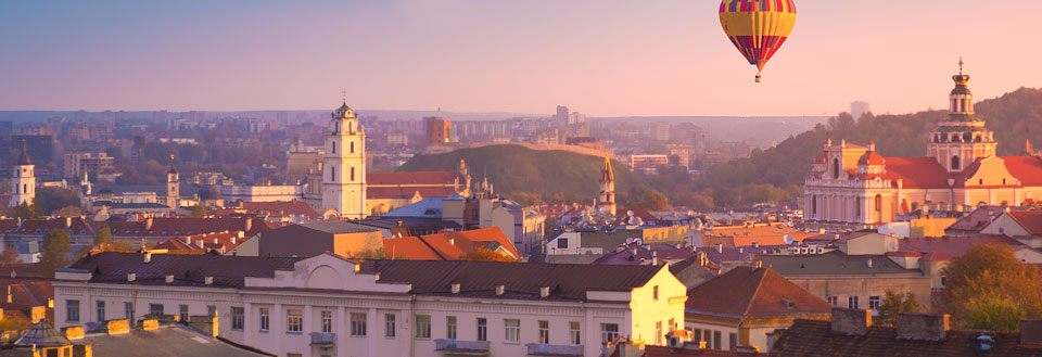 Vilnius ved solnedgang med kirker, gamle bygninger og en varmluftballon på himlen.