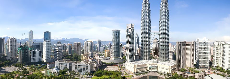 Kuala Lumpur med Petronas Towers, forskellige bygninger og grønne områder. Blå himmel i baggrunden.