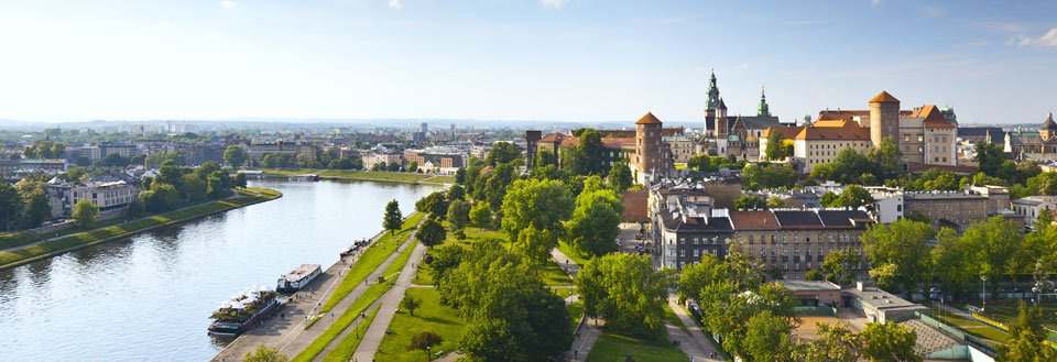 Panoramaudsigt over en europæisk by med en flod, grønne områder og historiske bygninger under en klar himmel.