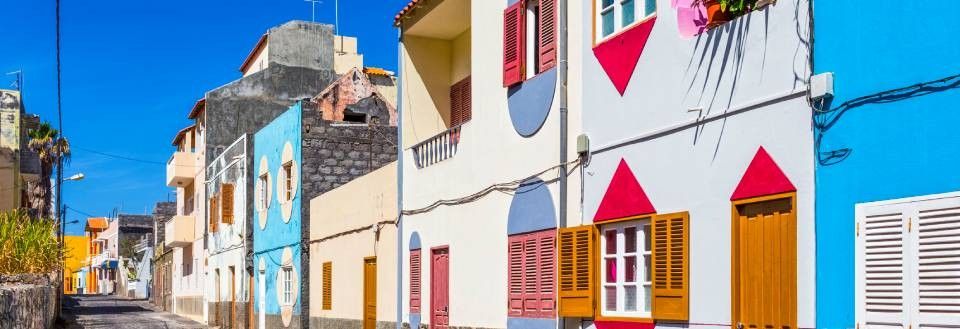 Billedet viser en farverig gade med traditionelle huse med farvestrålende facader og skodder under en klar blå himmel.
