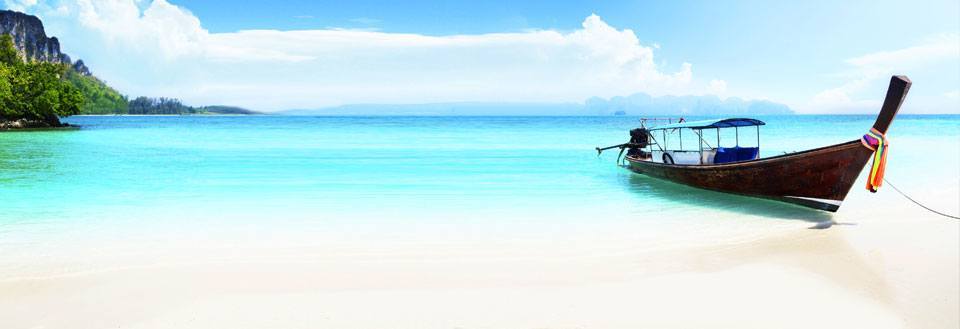 En traditionel langhalebåd ved en smuk tropisk strand med krystalklart vand og blå himmel.