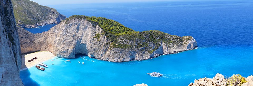 Panoramabillede af en idyllisk bugt med turkisblåt vand, omkranset af klipper og en strand.