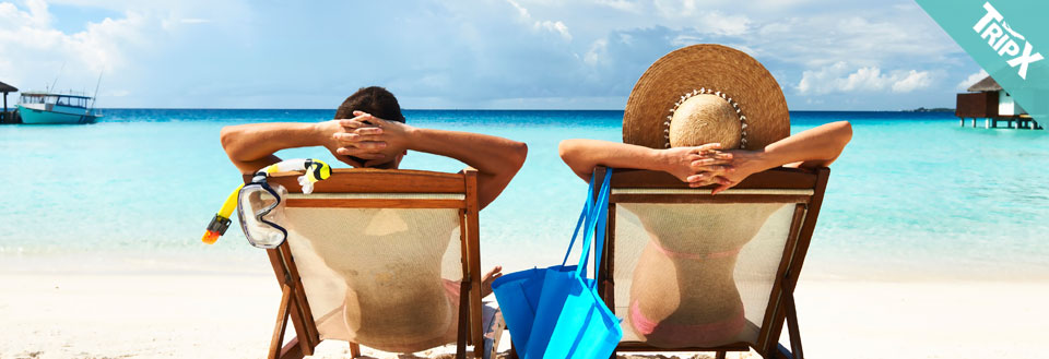 To personer slapper af i liggestole på en tropisk strand med klart blå vand.