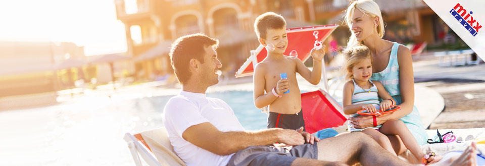 En familie nyder solen ved poolkanten, leger med legetøj og slapper af på liggestole.