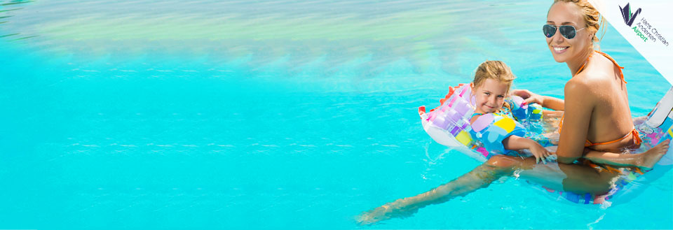 En kvinde og et barn smiler og nyder svømmetid i en pool med klart blåt vand.