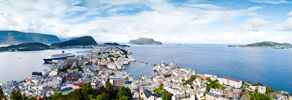 Panoramaudsigt over en kystby med farverige huse, et krydstogtskib i havnen og omkringliggende bjerge.