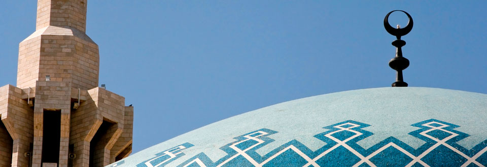Billedet viser toppen af en moskékuppel med karakteristisk ornamentik og en minaret ved siden af.