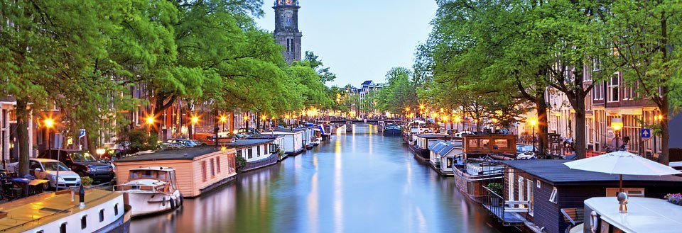 En billedskøn kanal med husbåde omgivet af træer og bygninger. Aftenbelysning skaber en hyggelig atmosfære.