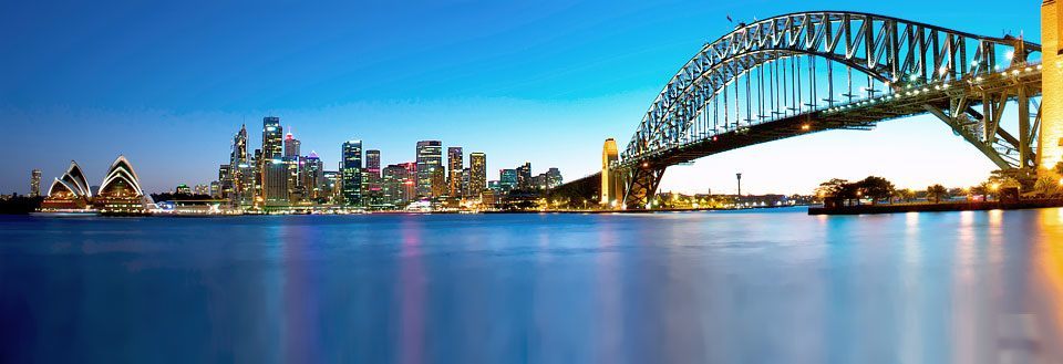 Panoramaudsigt over Sydney med Sydney Bridge og Utzons operahus i skumringen.